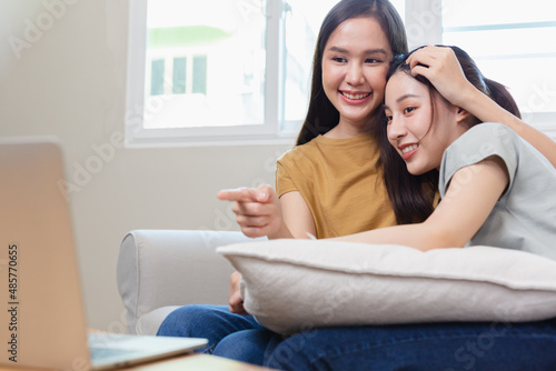 Happy asian women lesbian couple relax time watching movie media online on laptop in living room. homosexual couple hugging each other in love.