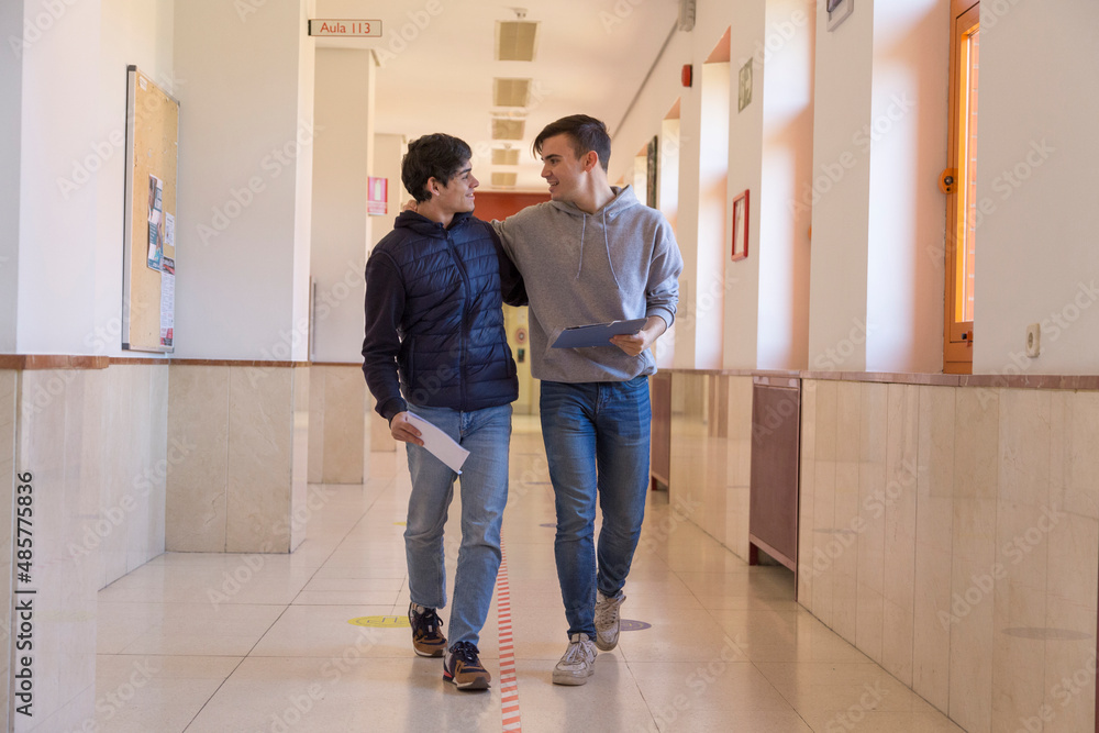 couple of gay university student friends walking down a corridor hugging each other