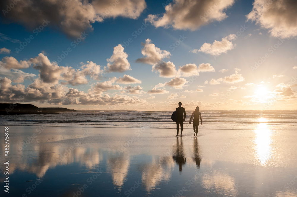 Fototapeta premium Couple surfing at Constantine Bay at sunset, Cornwall, England, United Kingdom, Europe