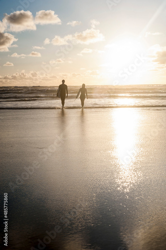 Photography Couple surfing at Constantine Bay at sunset, Cornwall, England, United Kingdom,