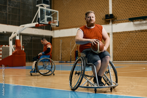 Disabled athlete in wheelchair on basketball sports court looking at camera.