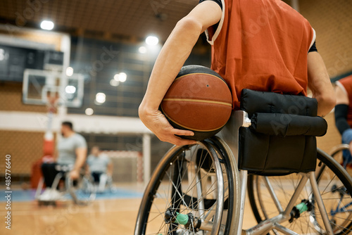 Rea view of handicapped basketball player in wheelchair holding a ball on sports court. © Drazen