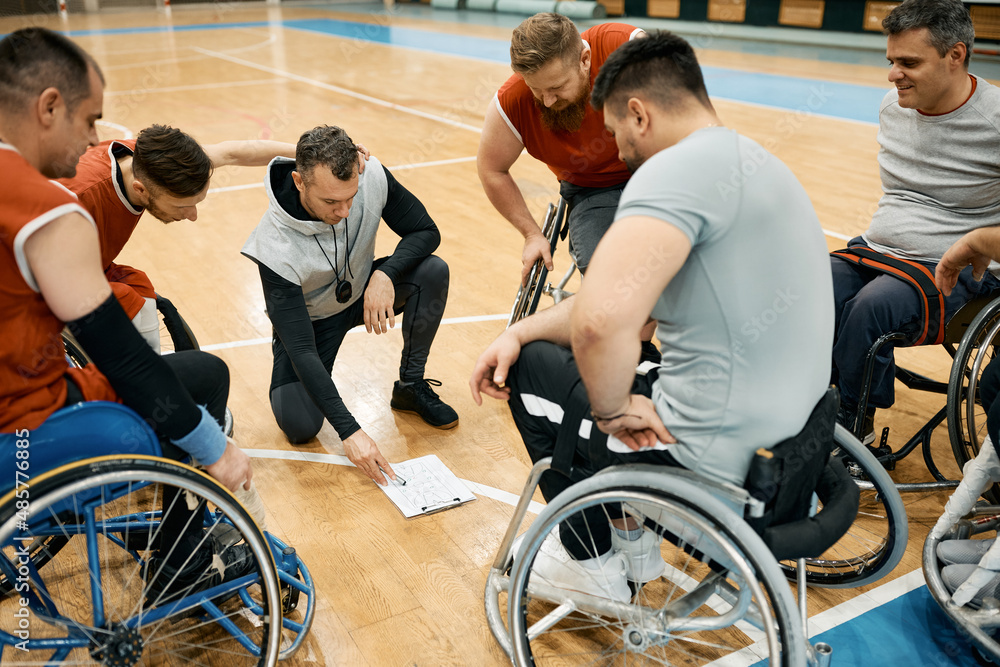 Wheelchair basketball coach explains game strategy to his players on the court. Wheelchair basketball coach explains game strategy to his players on the court.