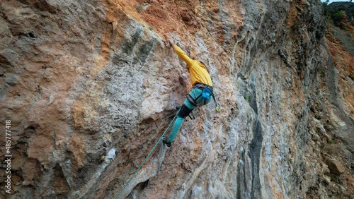 aerial slow motion back view strong man rock climber climbs on overhanging limestone cliff with tufas and colonets. sport and lifestyle outdoors photo