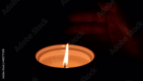 Closeup of hand moving close to a burning candle in dark background. photo