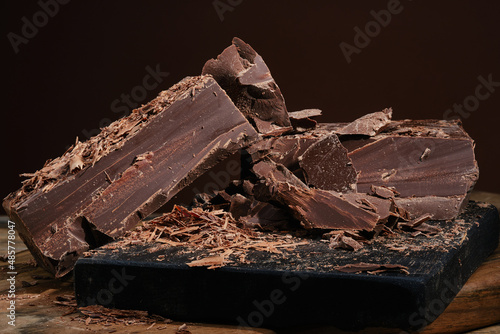 Composition of bars and pieces dark chocolate with chocolate chips on a wooden cutting board. Сrushed and chipped dark chocolate. Shallow depth of field.