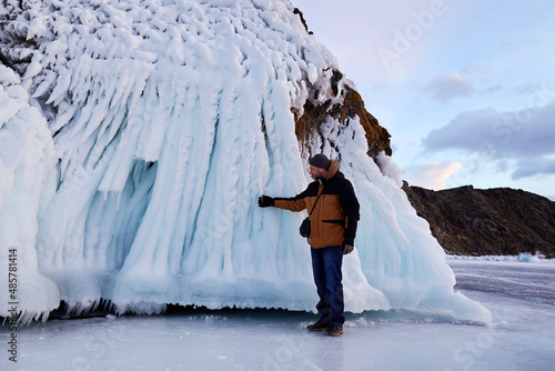 The man looks at the huge icicles on the rocks. Winter trip on the frozen lake Baikal. photo