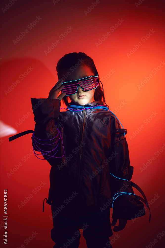 portrait cyberpunk boy child in neon glasses in blue and red tones with wires on a red background