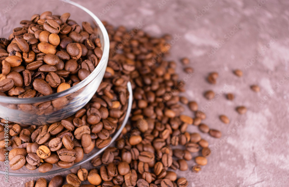 Lots of coffee beans in a transparent cup on a gray background.