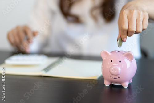 A woman puts coins in a piggy bank and writing a note in the financial book. Money saving concept.