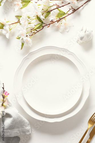 Easter festive dinner with golden eggs, festive tableware and flowers on white background. Top view. Festive tablescapes. Vertical format.