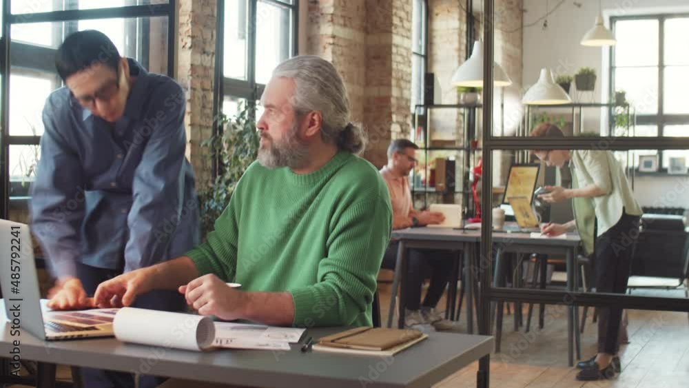 Time lapse of mature businessman working at desk in office he using laptop, reading documents, taking notes and communicating with colleagues Time lapse of mature businessman working at desk in office he using laptop, reading documents, taking notes and communicating with colleagues