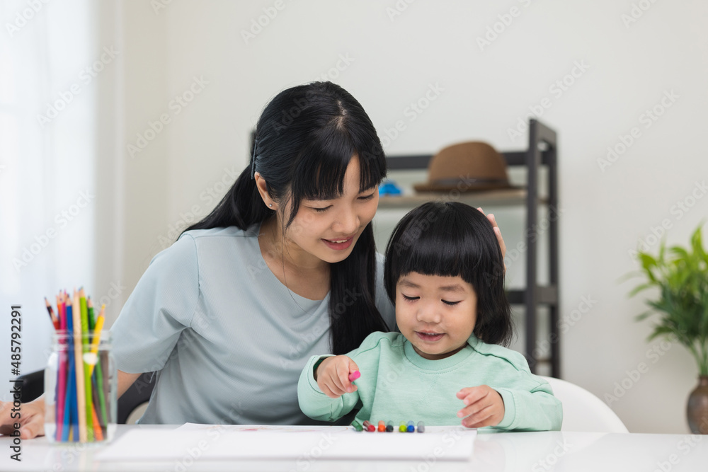Happy asian boy painting with crayon and colored pencil with his mother in living room at home. Mom teaching son how to painting with crayon color on book or doing homework. family concept. Happy asian boy painting with crayon and colored pencil with his mother in living room at home. Mom teaching son how to painting with crayon color on book or doing homework. family concept.