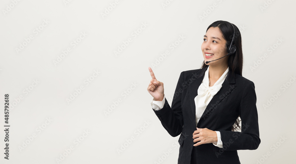 Happy young asian business woman call centre pointing finger to blank space. Welcome female operator put on smalltalk headphone standing on isolated white background. Happy young asian business woman call centre pointing finger to blank space. Welcome female operator put on smalltalk headphone standing on isolated white background.