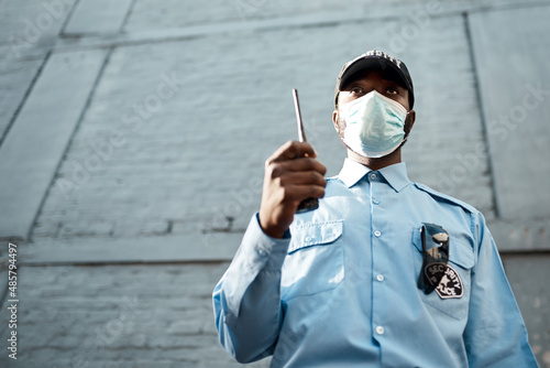 Proactive guarding for your propertys protection. Shot of a masked young security guard using a two way radio while on patrol outdoors. photo