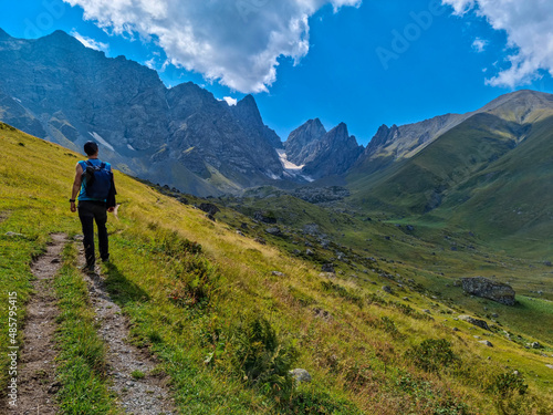 A man walking on a hiking trail with a view on the sharp mountain peaks of the Chaukhi massif in the Greater Caucasus Mountain Range in Georgia, Kazbegi Region. Remedy, Wanderlust.Georgian Dolomites