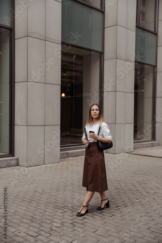  young designer woman with laptop and coffee of thew modern office building background