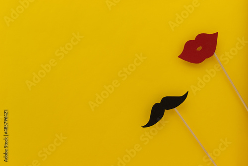 Black moustache and red lips made out of paper on wooden sticks castinf a shadow on a yellow background. photo