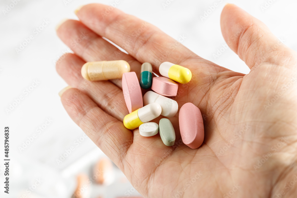 Aged female hand with pills on light background. Aged female hand with pills on light background.