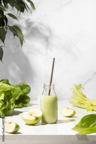 Green detox smoothies in a bottle standing on white table, front view