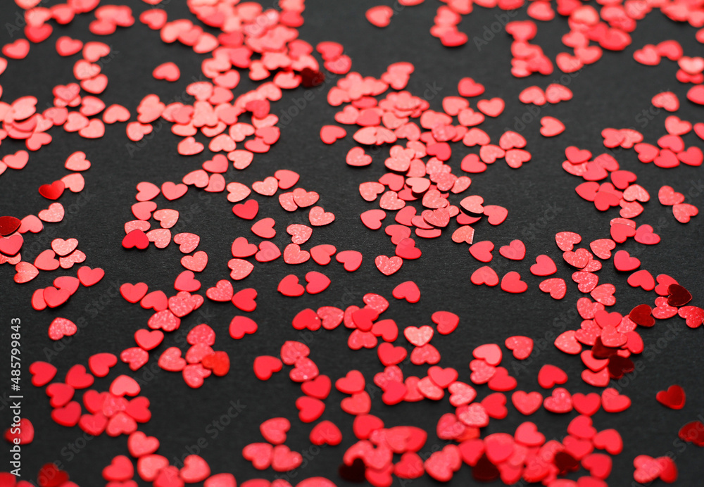 Scattered random red sequins in form of hearts on black textured background Scattered random red sequins in form of hearts on black textured background