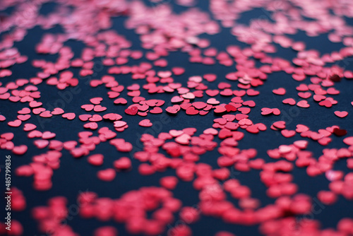 Scattered random red sequins in form of hearts on black textured background