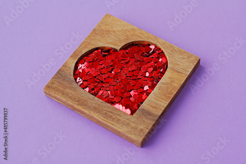 Wooden heart-shaped box with red sequins in form of hearts on purple background