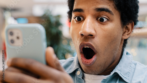 African american guy surprised by message received wins online bets looking at mobile phone opens mouth in surprise delighted shock man feels happiness from unexpected news amazing offer opportunity photo