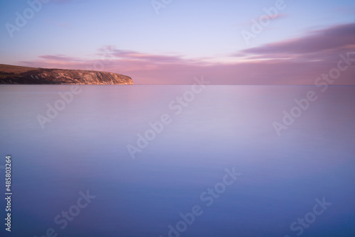Slow shutter speed image of the sea and horizon as the sun sets in Swanage. Smooth calm ocean water with pink blue and purple colours at sunset in the UK