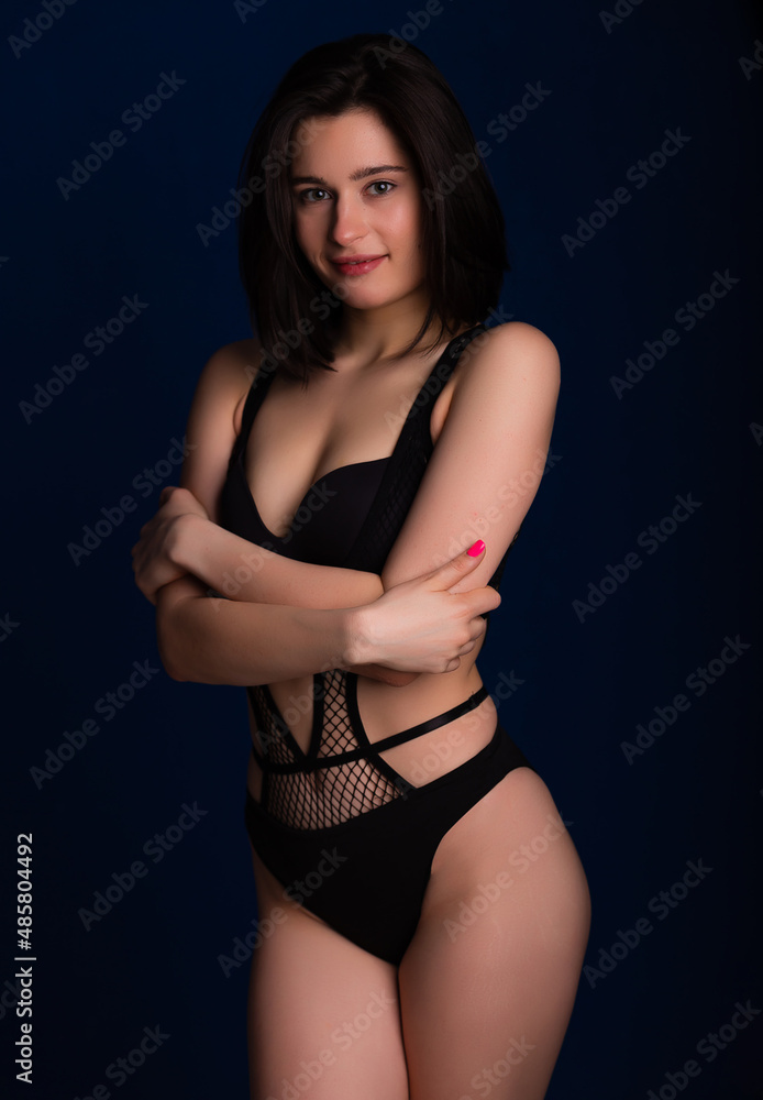Fototapeta premium Woman posing in seductive black lingerie. Attractive beauty lady advertising underwear slim body on dark blue background free space for text