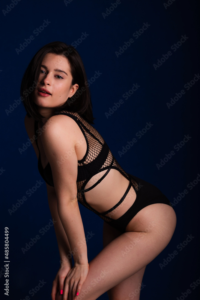 Fototapeta premium Woman posing in seductive black lingerie. Attractive beauty lady advertising underwear slim body on dark blue background free space for text