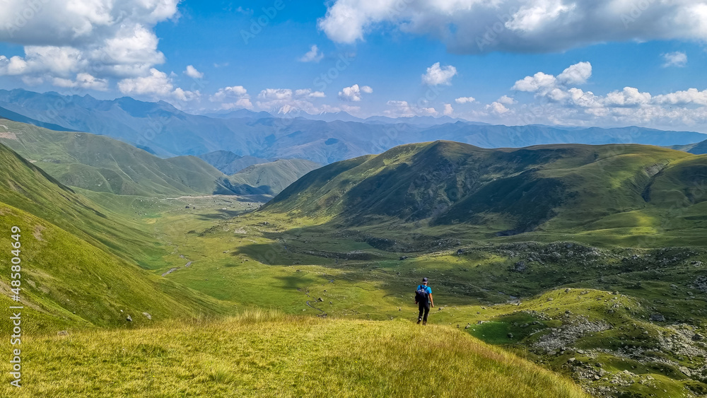 A man walking on a hiking trail with a view on green hills near the Chaukhi Pass in the Greater Caucasus Mountain Range in Georgia, Kazbegi Region. Remedy, Wanderlust.Georgian Dolomites