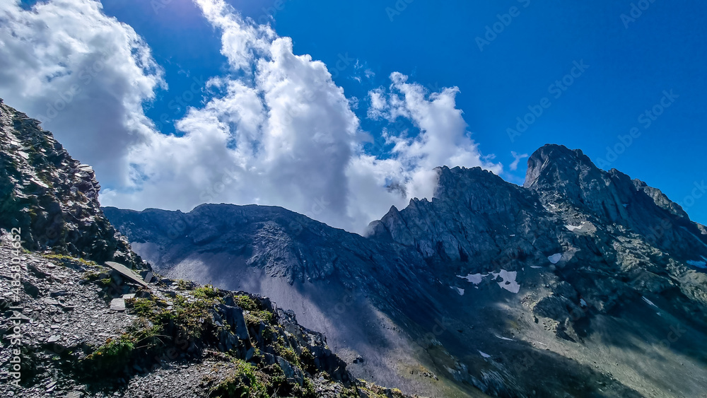 Clouds accumulating around the sharp mountain peaks of the Chaukhi massif in the Greater Caucasus Mountain Range in Georgia, Kazbegi Region. Mountain Ridges, Hiking. Georgian Dolomites. Cloudscape