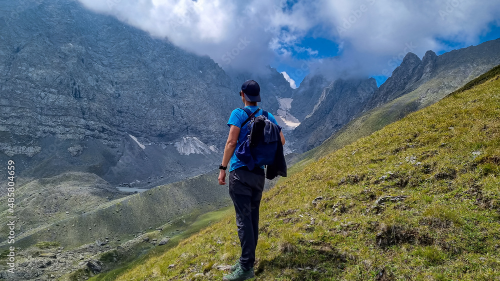 A man walking on a hiking trail with a view on the sharp mountain peaks of the Chaukhi massif in the Greater Caucasus Mountain Range in Georgia, Kazbegi Region. Remedy, Wanderlust.Georgian Dolomites