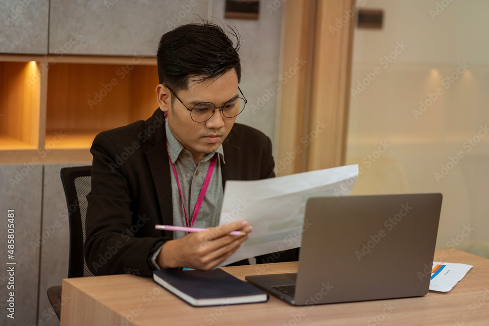 male worker in a suit holding a validation document sits at a laptop at his desk in a home office. male worker in a suit holding a validation document sits at a laptop at his desk in a home office.