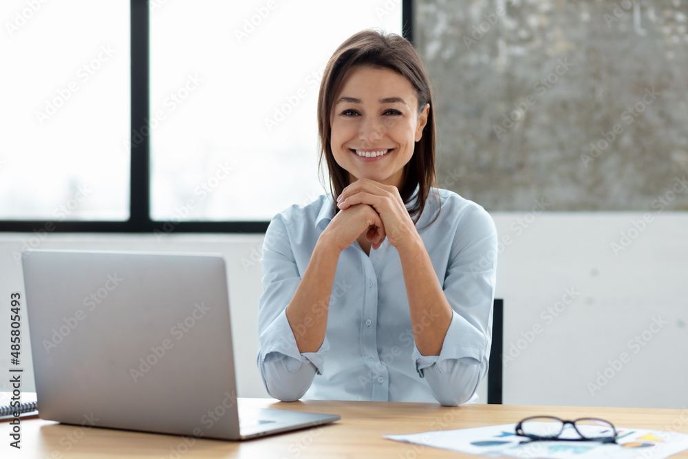 Happy portrait of successful confident business woman sitting at the table in the office looks at the camera and smiling in friendly Happy portrait of successful confident business woman sitting at the table in the office looks at the camera and smiling in friendly