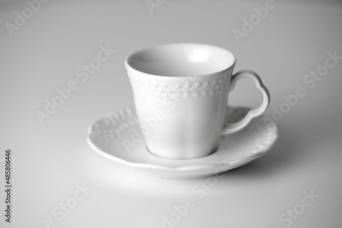 White tea cup and saucer with a pattern for drink on white background. Ceramic coffee cup or mug close up. Mockup classic porcelain utensils. copy space