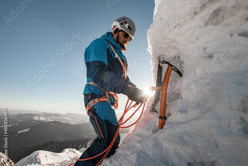view of ice axe and man climber with equipment and ropes on the slope against backdrop of sky