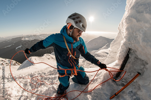 man with climbing equipment fixes rope on mountain slope against the backdrop of landscape and sky