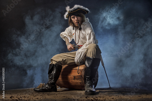 Konstfotografi Pirate filibuster sea robber in suit with gun and saber sits on barrel
