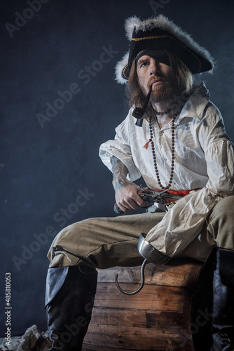 Billede på lærred Pirate filibuster sea robber in suit with gun and saber sits on barrel