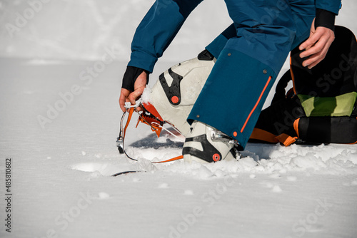 Close-up of leg of man wearing climbing crampons over mountaineering shoes for walking through glacier.