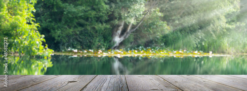 empty wooden jetty planks in front of a blurred water idyll background with wild vegetation in sunlight, beautiful summertime in nature lakeside, concept with advertising space