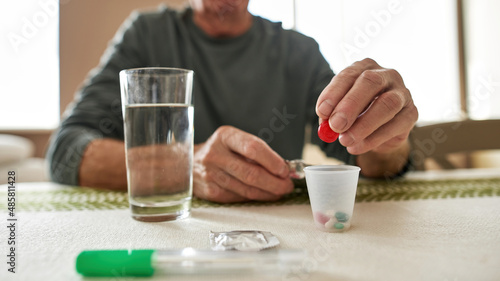 Focus on sick man hand putting pill in plastic cup