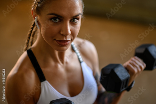 Young attractive woman training outside while using dumbbells and airpods