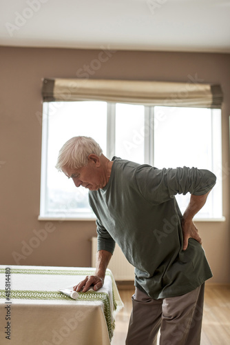 Grey hair man with backache standing near table