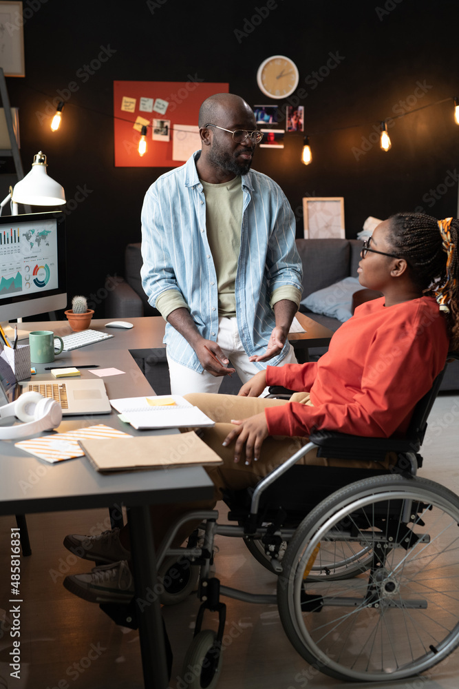 African woman sitting on wheelchair and discussing the work with her colleague at office African woman sitting on wheelchair and discussing the work with her colleague at office