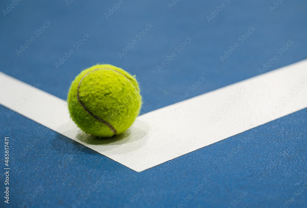 Tennis ball on white line on blue hard tennis court. Close-up.