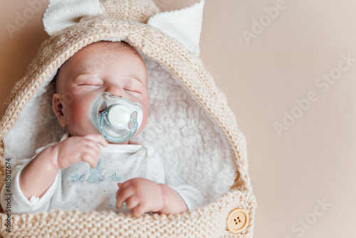 Bild auf Leinwand Reborn a boy doll with a pacifier sleeps in a knitted beige envelope