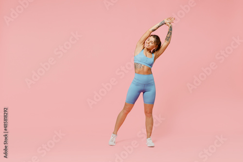Fototapeta Naklejka Na Ścianę i Meble -  Full body young sporty fitness trainer woman wear blue tracksuit spend time in home gym tilt body to sides with hand stretch lunge exercise isolated on plain pink background. Workout sport concept